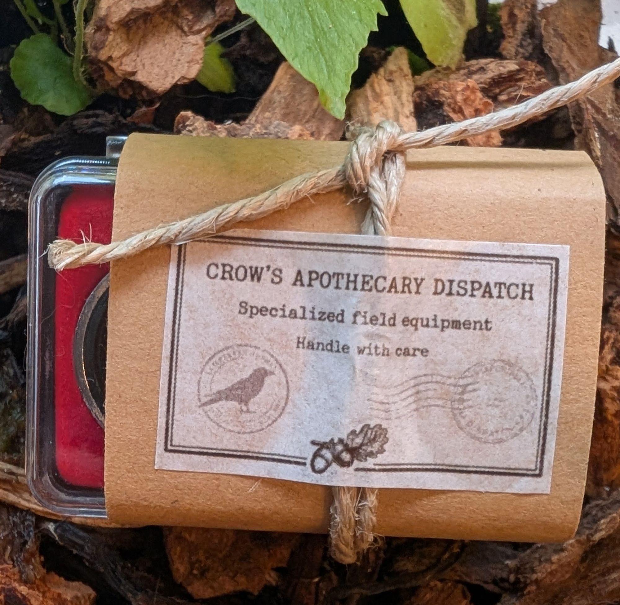 A kraft-wrapped field kit tied with twine on bark, with a red-lined tin and a typewritten Crow’s Apothecary Dispatch label